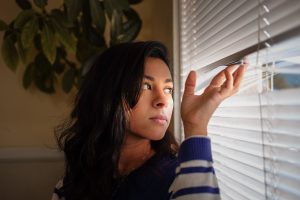 A woman looks apprehensive and looks tentatively out of her window.